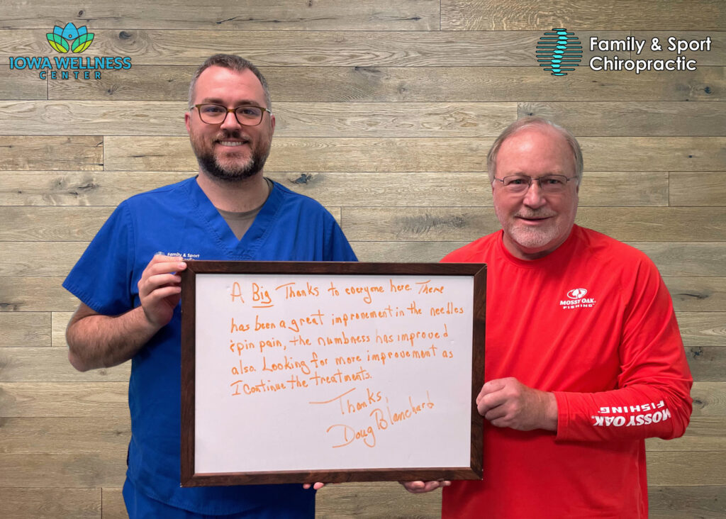 A physical rehabilitation doctor near Iowa City stands next to patient holding a whiteboard that states how he found relief from neuropathy at the wellness center
