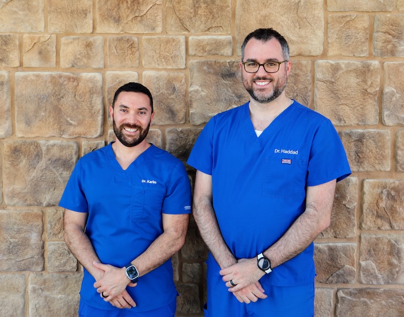 Two chiropractors wearing blue scrubs stand in front of wall to pose for photo that will appear on site for physical rehabilitation doctor near Iowa City