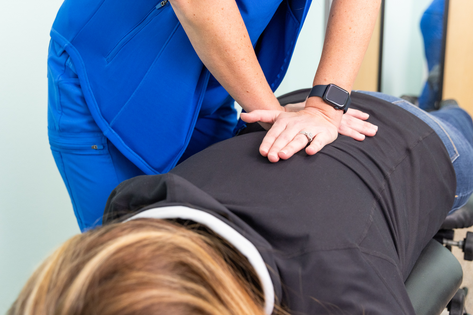 Chiropractor's hands placed strategically on patient's back for a spinal adjustment to relieve back pain. This is part of a comprehensive weight loss program near Cedar Rapids.