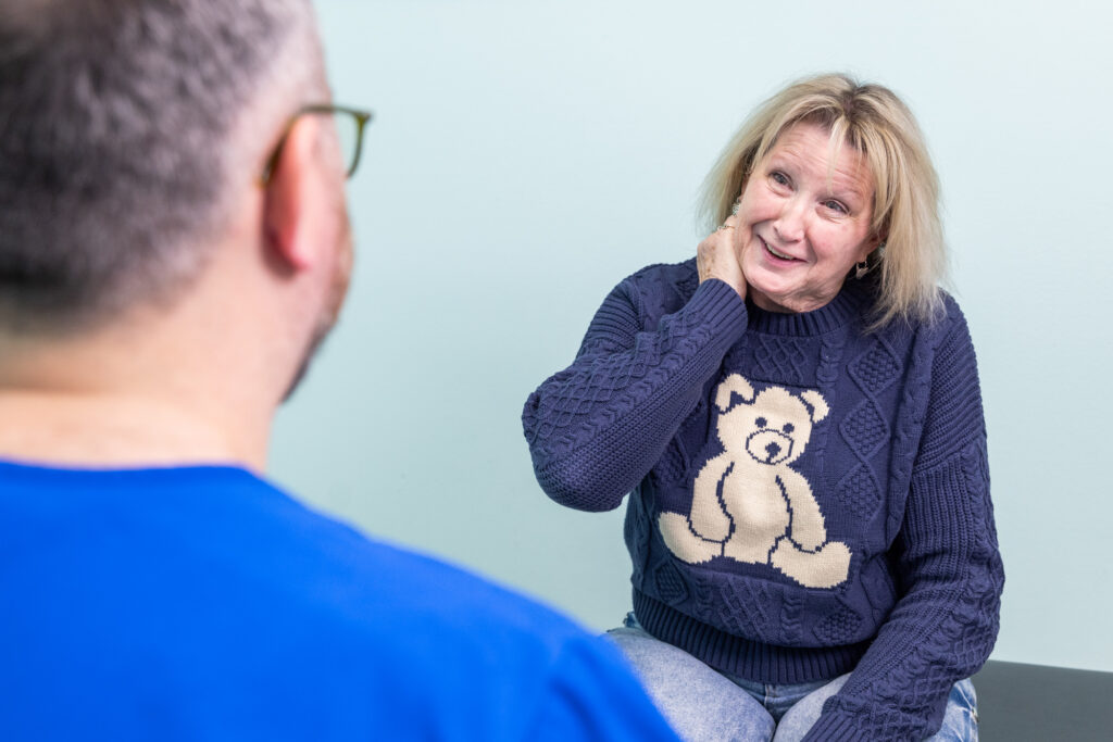 Woman in chiropractic office looks at doctor and holds hand to neck, explaining where she feels pain to learn about her options for neck pain relief near Iowa City