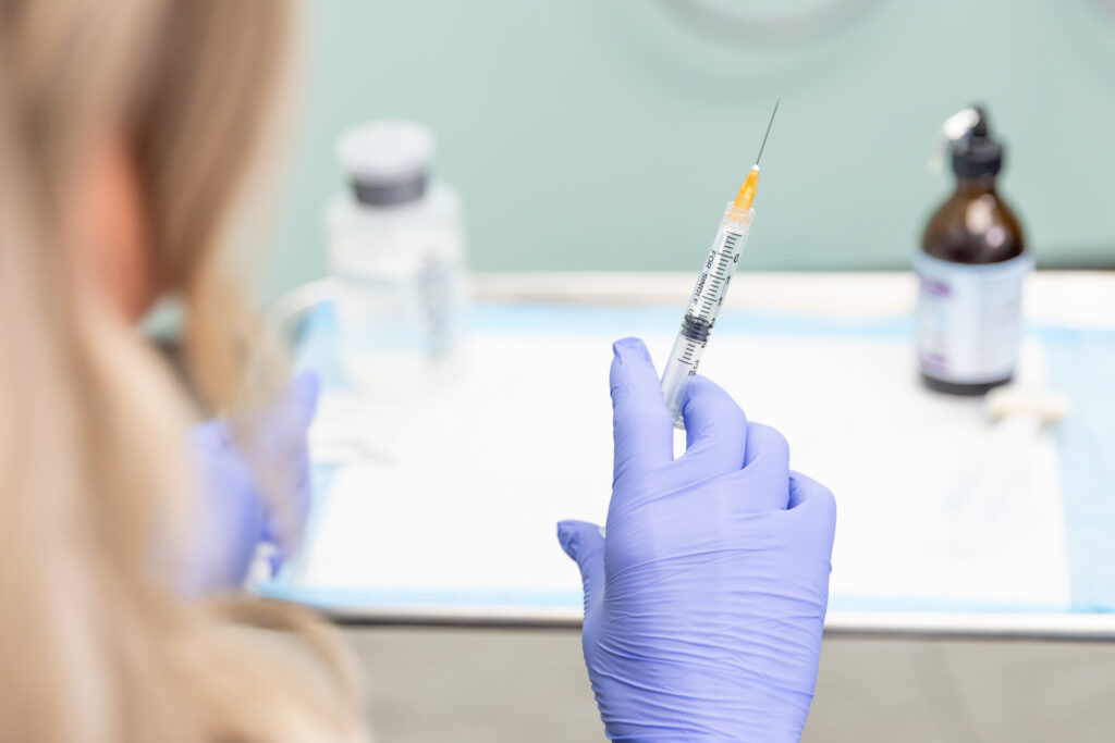 Chiropractor wearing gloves holds a syringe containing an ozone and oxygen gas mixture which she will inject into her patient's body to reduce inflammation and joint pain.