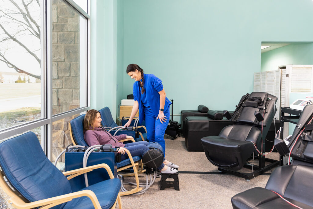 Woman receives physical therapy near Iowa City for chronic back pain. She sits in specialized chair to improve spinal discomfort while a chiropractor stands over her and monitors the treatment.
