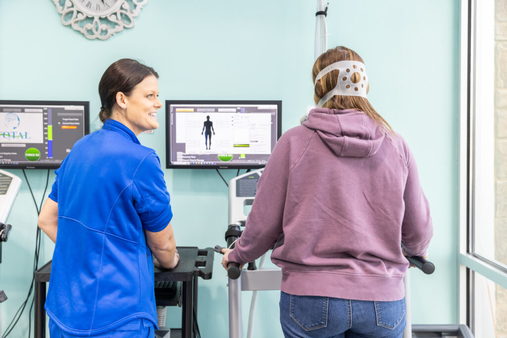 Woman stands on treadmill and sees body composition information on screen in front of her. A chiropractor explains how this alleviates her chronic pain and is part of her treatment plan for physical therapy near Iowa City.