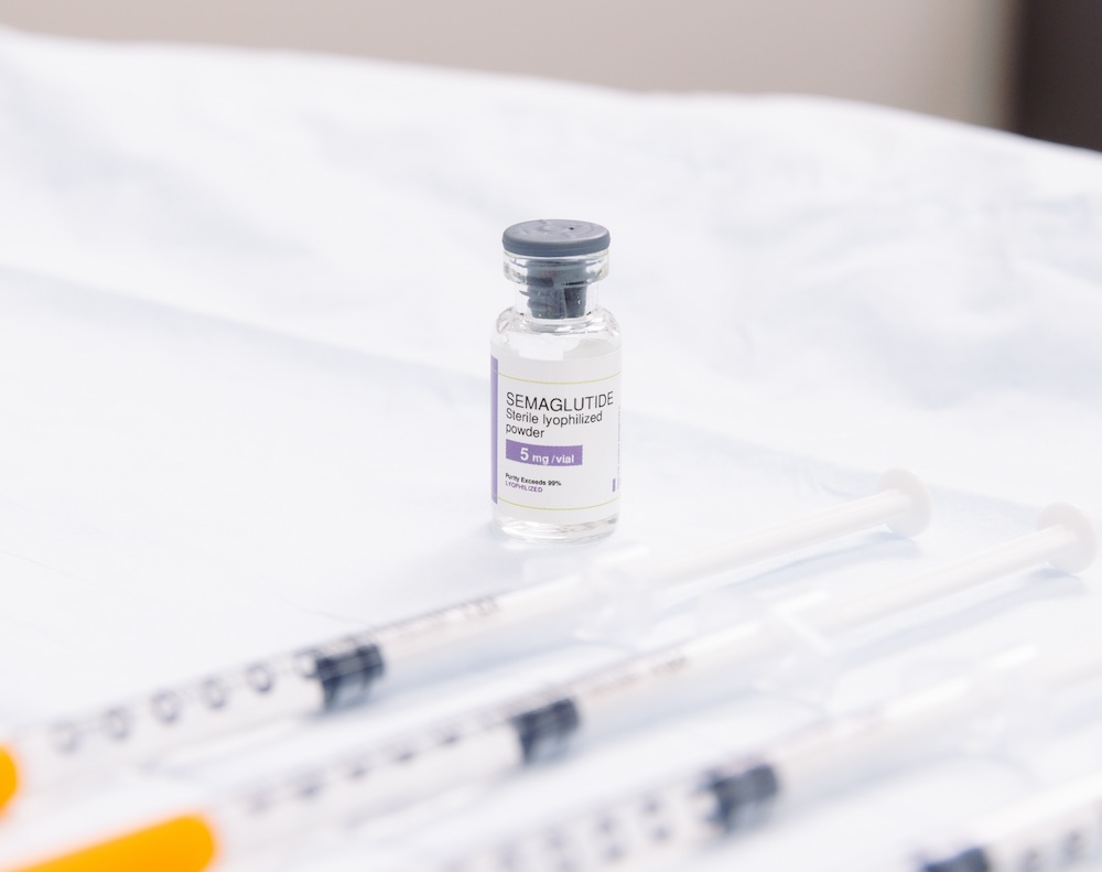 Bottle of semaglutide sitting on table with 4 syringes placed neatly in order. This is a weight loss medication people also recognize as a GLP-1 near Iowa City.