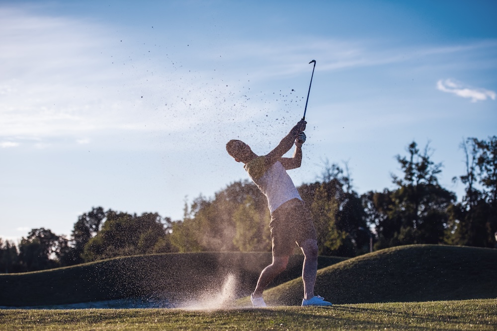 Guy on golf course swinging his club after hitting a golf ball. He has improved performance now that he regularly receives a sports massage in North Liberty