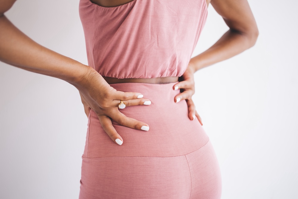 Woman places hands on lower back and tries to alleviate pain radiating up her spine. She's about to go to a physical therapist for disc herniation treatment in North Liberty.