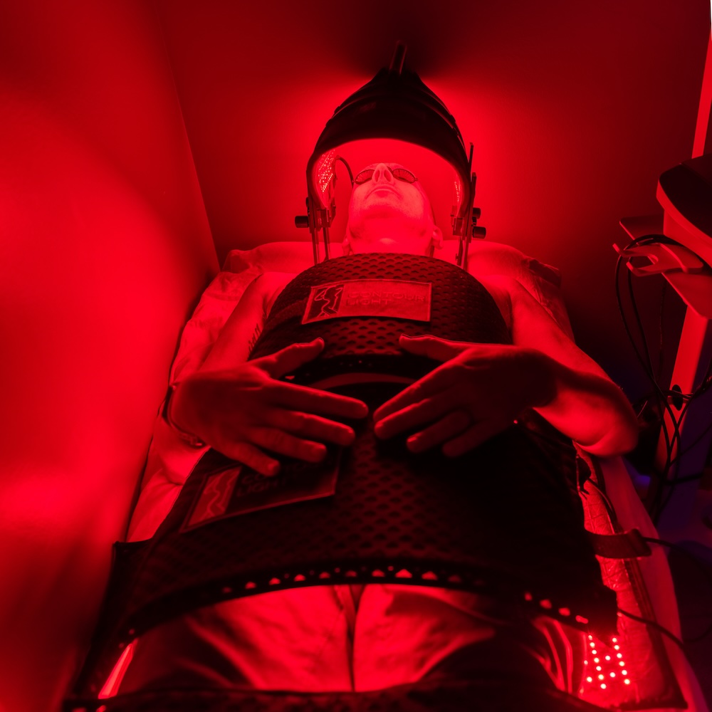 Patient lays on back in a room where they are receiving red light therapy. This is one of many answers to the question of "how to reduce inflammation in the body." The red light stimulates cellular function to reduce pain and increase energy.